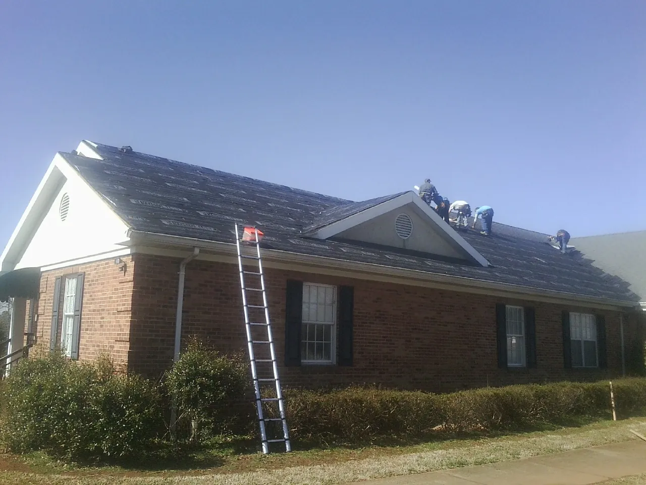 Crew tearing shingles off a brick ranch roof with a ladder set — Emergency Roof Repair work by our crew in Chemult