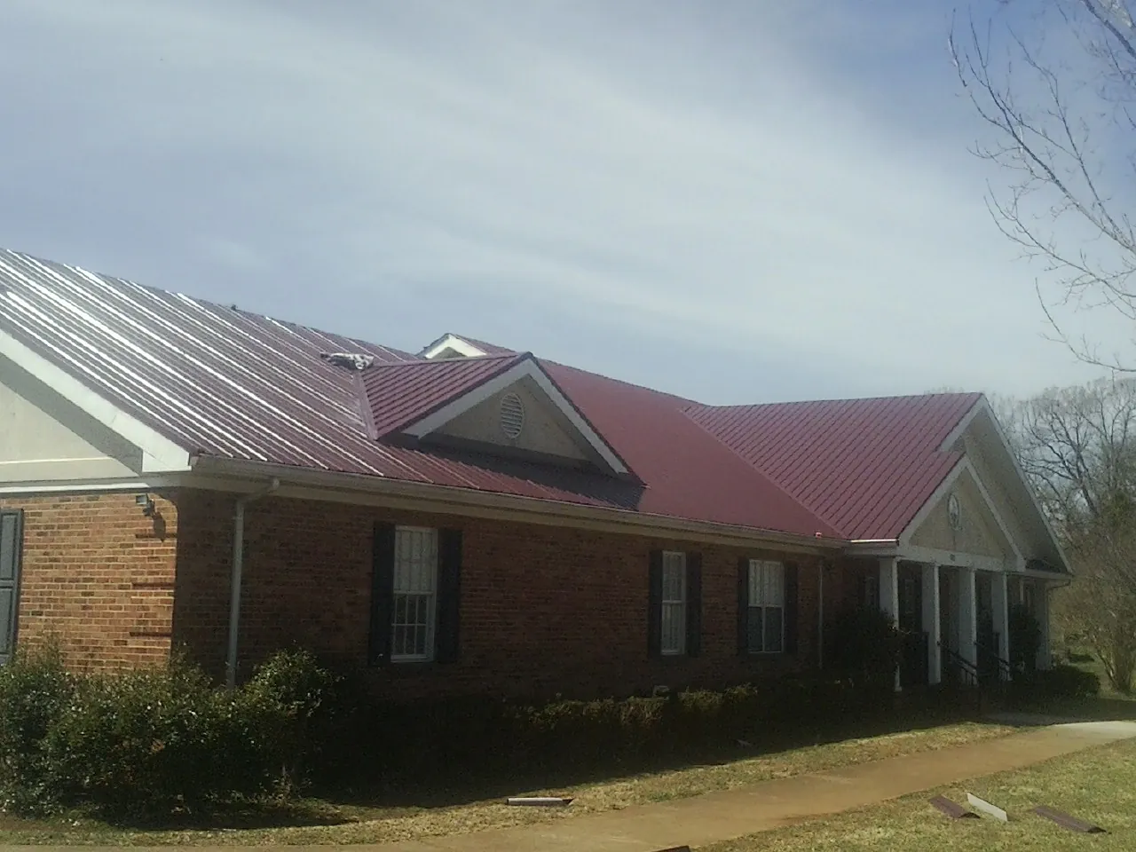 Red metal roof with gabled entries on a long brick building, from a Hail Damage Roof Repair job in Chemult