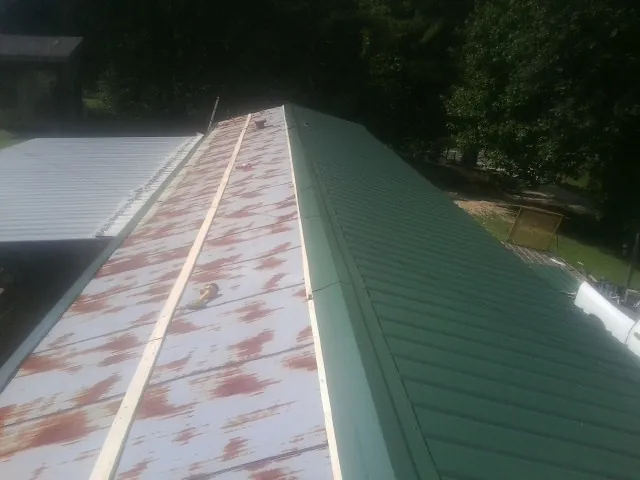 Old rusted panels beside newly installed green metal roofing — Wind Damage Roof Repair by Roofing Brothers in Chemult