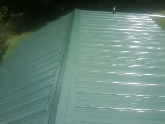 New green metal panels meeting at the ridge of a roof — Flat Roof Repair work by our crew in Chemult
