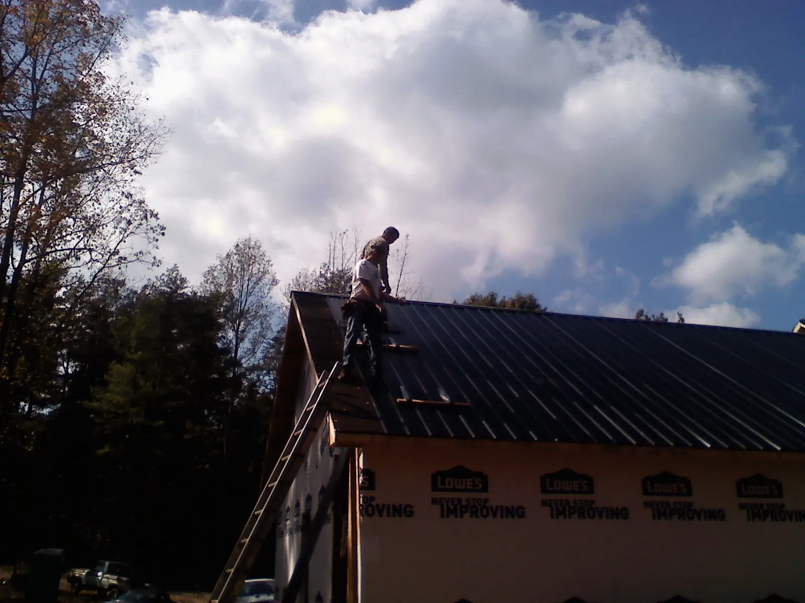 Roofer fastening dark metal panels high against a cloudy sky, from a Roof Inspection job in Chemult