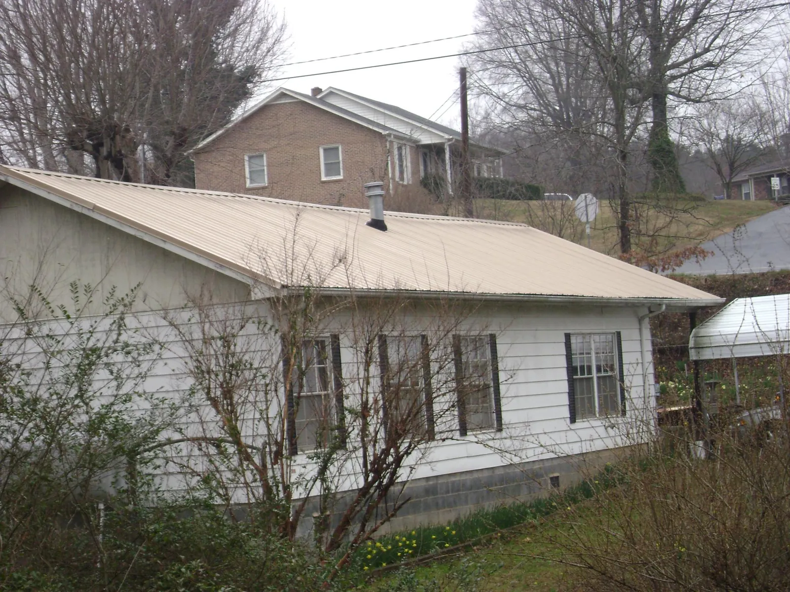 Tan metal roof on a white sided house set into a hillside — Commercial Roofing by Roofing Brothers in Chemult